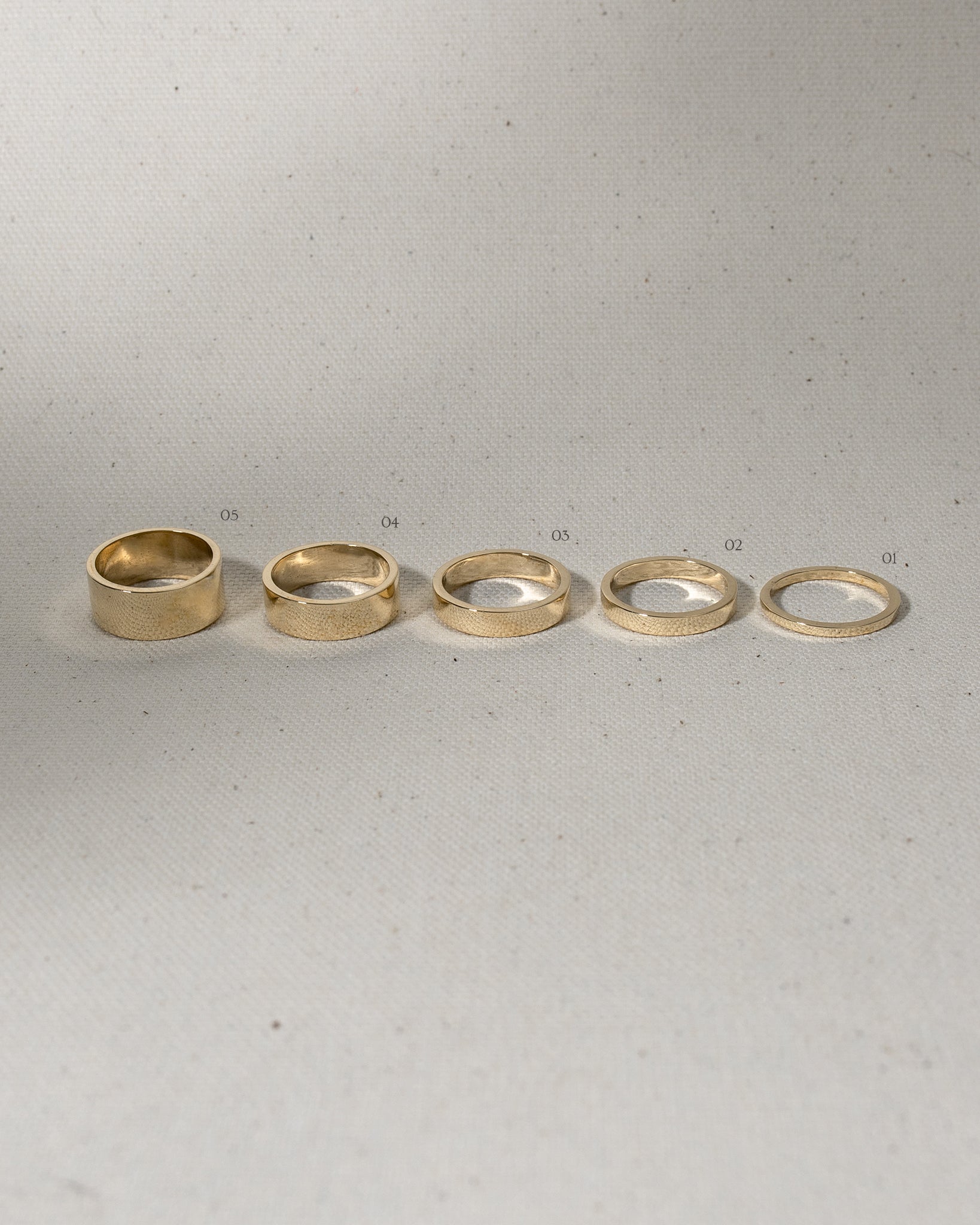 Selection of 5 different width flat gold rings on canvas