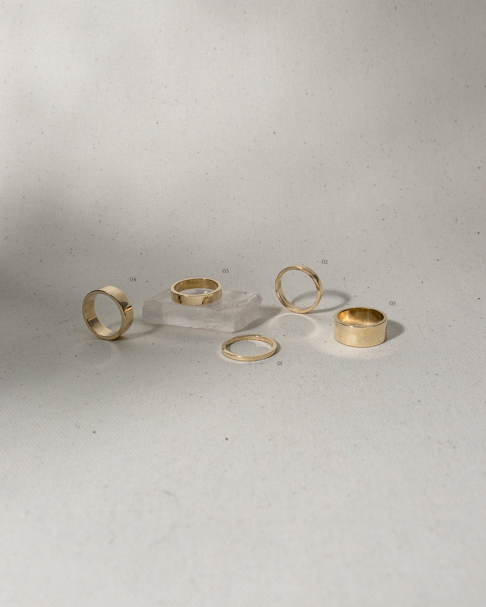 Selection of 5 different width flat gold rings on canvas